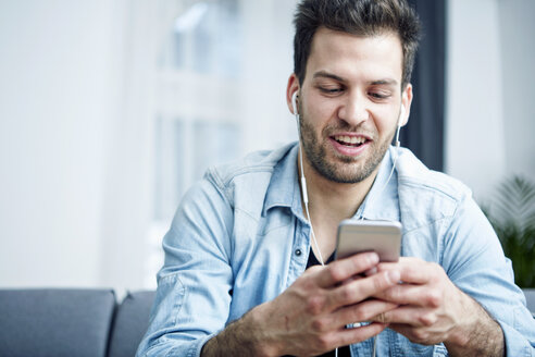 Young man at home with smartphone and earbuds - SEGF000439