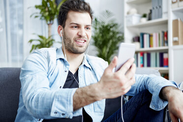 Young man at home with smartphone and earbuds - SEGF000440