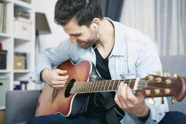 Junger Mann sitzt zu Hause auf der Couch und spielt Gitarre - SEGF000449