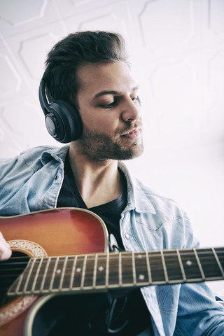 Junger Mann trägt Kopfhörer und spielt Gitarre, lizenzfreies Stockfoto