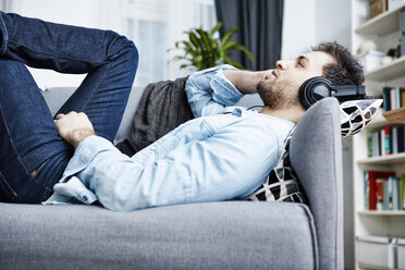 Junger Mann zu Hause auf der Couch liegend mit Kopfhörern - SEGF000456