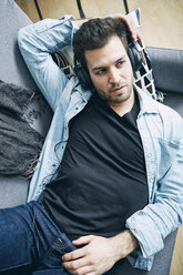 Young man at home lying on couch wearing headphones - SEGF000457