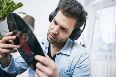 Young man wearing headphones looking at record - SEGF000462