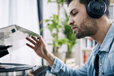 Young man wearing headphones starting record player - SEGF000467