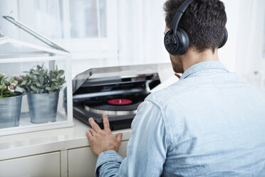 Young man wearing headphones starting record player - SEGF000468