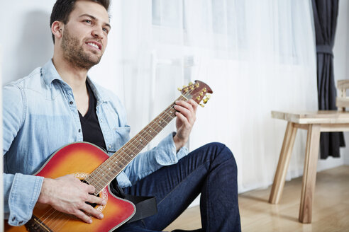 Young man sitting on floor playing guitar - SEGF000470