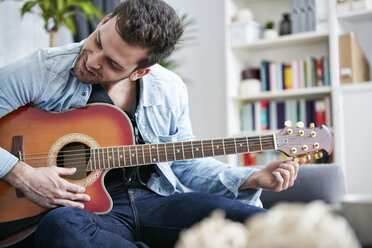 Junger Mann sitzt auf der Couch und stimmt Gitarre - SEGF000475