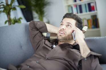 Junger Mann spricht mit Smartphone auf der Couch liegend - SEGF000483