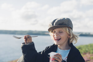 Frankreich, Bretagne, Atlantik, glücklicher Junge an der Küste, der Joghurt isst - MJF001774