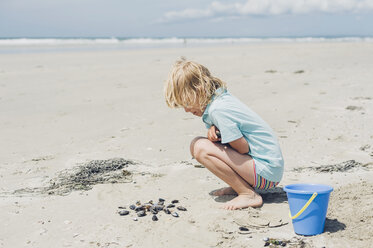 Frankreich, Bretagne, Finistere, Pointe de la Torche, Junge spielt mit Muscheln am Strand - MJF001785