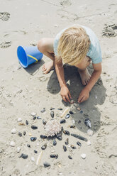 Frankreich, Bretagne, Finistere, Pointe de la Torche, Junge spielt mit Muscheln am Strand - MJF001786