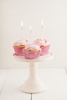Three pink cup cakes with lighted birthday candles on a cakestand - ECF001850
