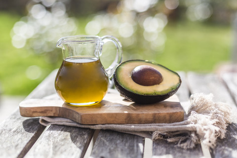 Eine halbe Avocado und ein Glaskrug mit Avocadoöl auf einem Holzbrett, lizenzfreies Stockfoto