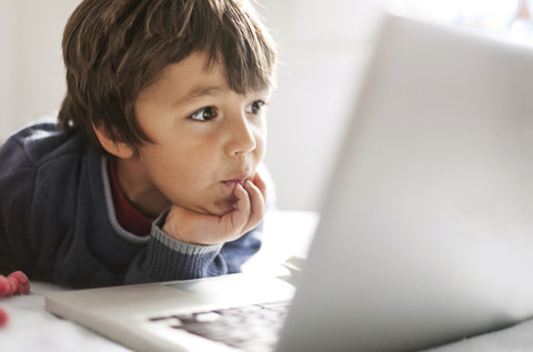 Porträt eines kleinen Jungen, der auf einen Laptop starrt, lizenzfreies Stockfoto