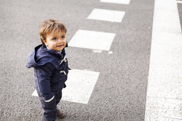 Porträt eines lächelnden kleinen Jungen, der auf einer Straße steht und nach oben schaut - VABF000228