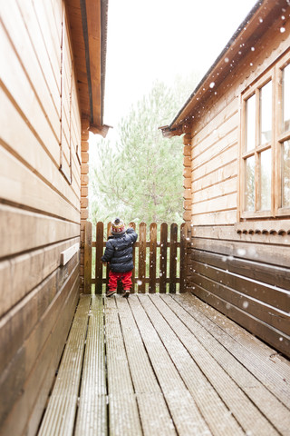 Rückenansicht eines kleinen Jungen, der zwischen zwei Blockhütten im Winter steht, lizenzfreies Stockfoto