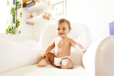 Smiling baby boy with diapers sitting on an armchair - VABF000235