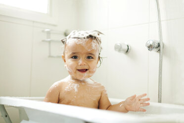 Portrait of smiling baby boy with foam in his hair sitting in bathtub - VABF000237