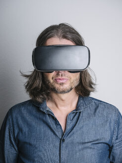 Porträt eines Mannes, der eine Virtual-Reality-Brille vor einem grauen Hintergrund trägt - KRPF001734