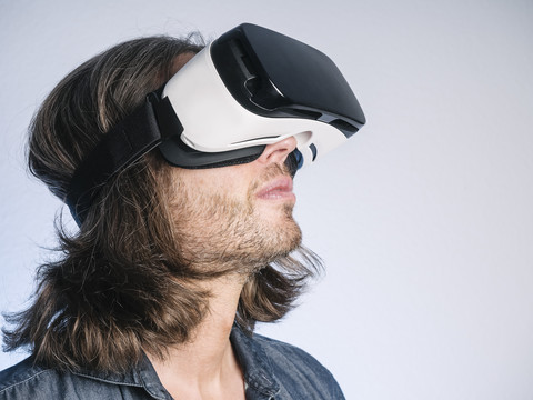 Man wearing Virtual Reality Glasses looking up in front of grey background stock photo