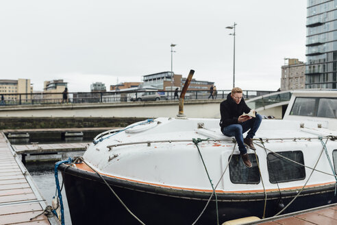 Ireland, Dublin, young man sitting on a motorboat reading a book - BOYF000099