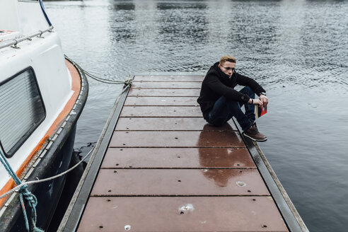 Young man with book cowering on a jetty in winter - BOYF000100