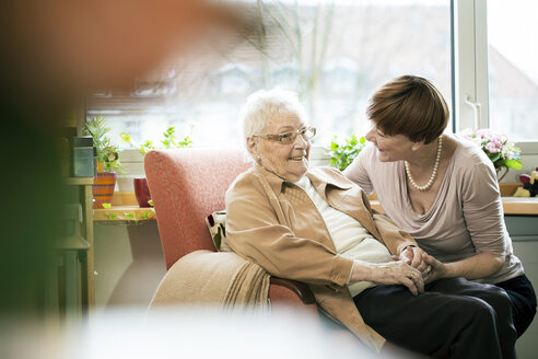 Adult daughter talking to her mother with Alzheimer's disease in her room at retirement home - JATF000849