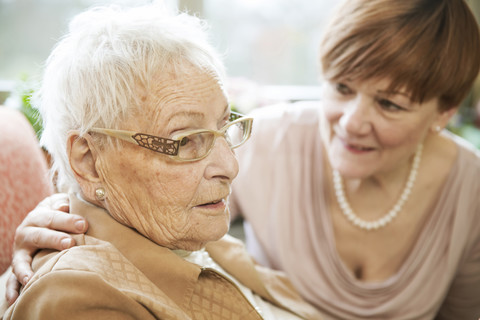 Portrait of senior woman with Alzheimer's disease with her adult daughter watching in the background stock photo