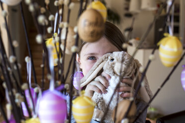 Girl hiding behind Easter bunny and twigs of willows decorated with Easter eggs - SARF002605