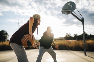 Zwei junge Männer spielen Basketball auf einem Platz im Freien - JRFF000485