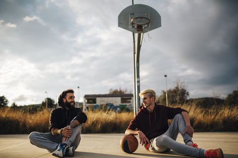 Zwei junge Männer sitzen auf einem Basketballplatz im Freien, lizenzfreies Stockfoto