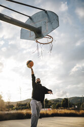 Young man playing basketball on an outdoor court - JRFF000489