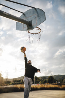 Junger Mann spielt Basketball auf einem Platz im Freien - JRFF000489