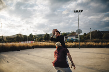 Zwei junge Männer spielen Basketball auf einem Platz im Freien - JRFF000490