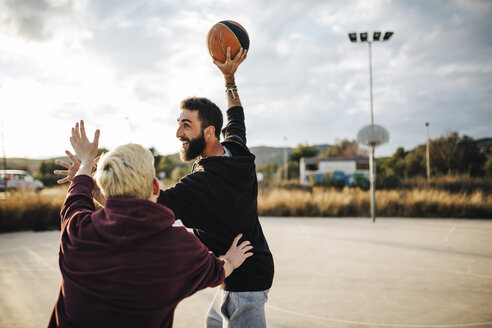 Zwei junge Männer spielen Basketball auf einem Platz im Freien - JRFF000491