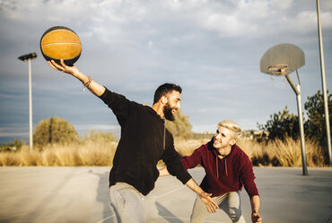 Zwei junge Männer spielen Basketball auf einem Platz im Freien - JRFF000492