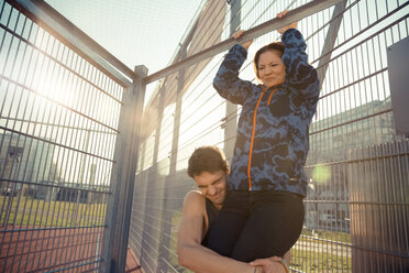 Young man helping girlfriend doing chin-ups - SUF000071