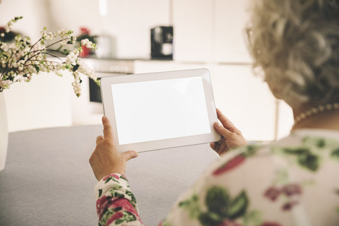 Blick über die Schulter auf eine ältere Frau, die zu Hause einen Tablet-Computer benutzt, lizenzfreies Stockfoto