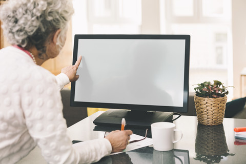 Blick über die Schulter auf eine ältere Frau, die zu Hause einen Desktop-Computer benutzt, lizenzfreies Stockfoto