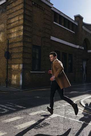 Junger Mann in Eile beim Überqueren einer städtischen Straße, lizenzfreies Stockfoto