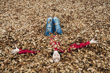 Woman with arms outstretched lying on forest soil covered with autumn leaves - GEMF000765