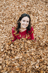 Porträt einer lächelnden Frau, die auf einem mit Herbstblättern bedeckten Waldboden sitzt - GEMF000768