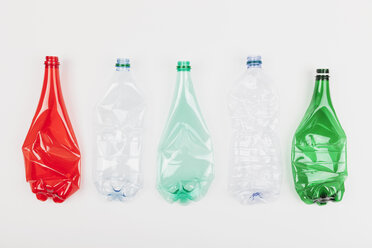 Row of five different empty flexed plastic bottles on white ground - GWF004641