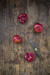 Two whole and two halves of organic pomegranate and a pocket knife on wood - LVF004583