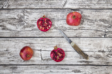 Two whole and two halves of organic pomegranate and a pocket knife on wood - LVF004587