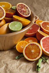 Wooden bowl of citrus fruits on crumpled brown paper - VABF000259