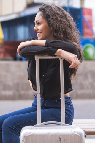 Lächelndes Teenager-Mädchen, das sich auf den Griff ihres Koffers stützt, lizenzfreies Stockfoto