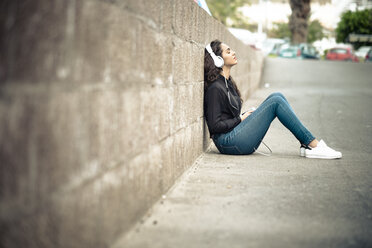 Teenage girl leaning against wall listening music with headphones - SIPF000219