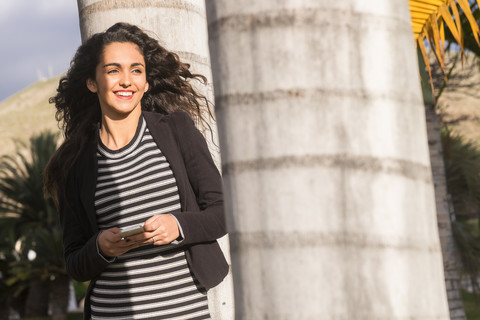 Spanien, Teneriffa, Porträt eines lächelnden Teenagers mit Smartphone, lizenzfreies Stockfoto