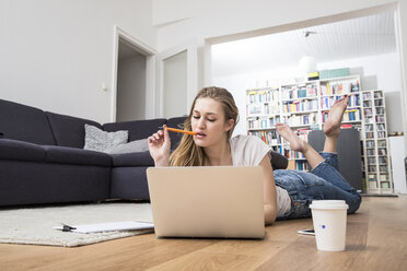 Junge Frau zu Hause auf dem Boden liegend mit Laptop - FMKF002415